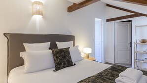 Ein ordentlich bezogenes Bett mit weißen Laken, einer gemusterten Tagesdecke, einer Nachttischlampe und einem Holz-Kopfstück.