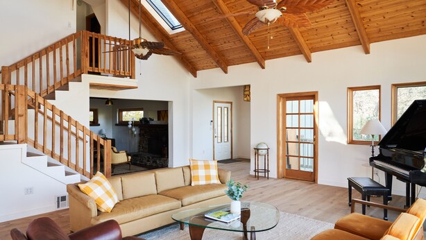 Un salón amplio con una escalera de madera, un piano y un ventanal grande.