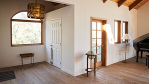 Una habitación amplia con suelos de madera, un piano, un globo terráqueo sobre un atril y un gran ventanal que proporciona luz natural.