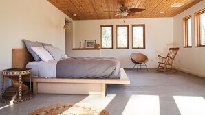 Un dormitorio con una cama, un ventilador de techo, una silla y ventanas amplias.