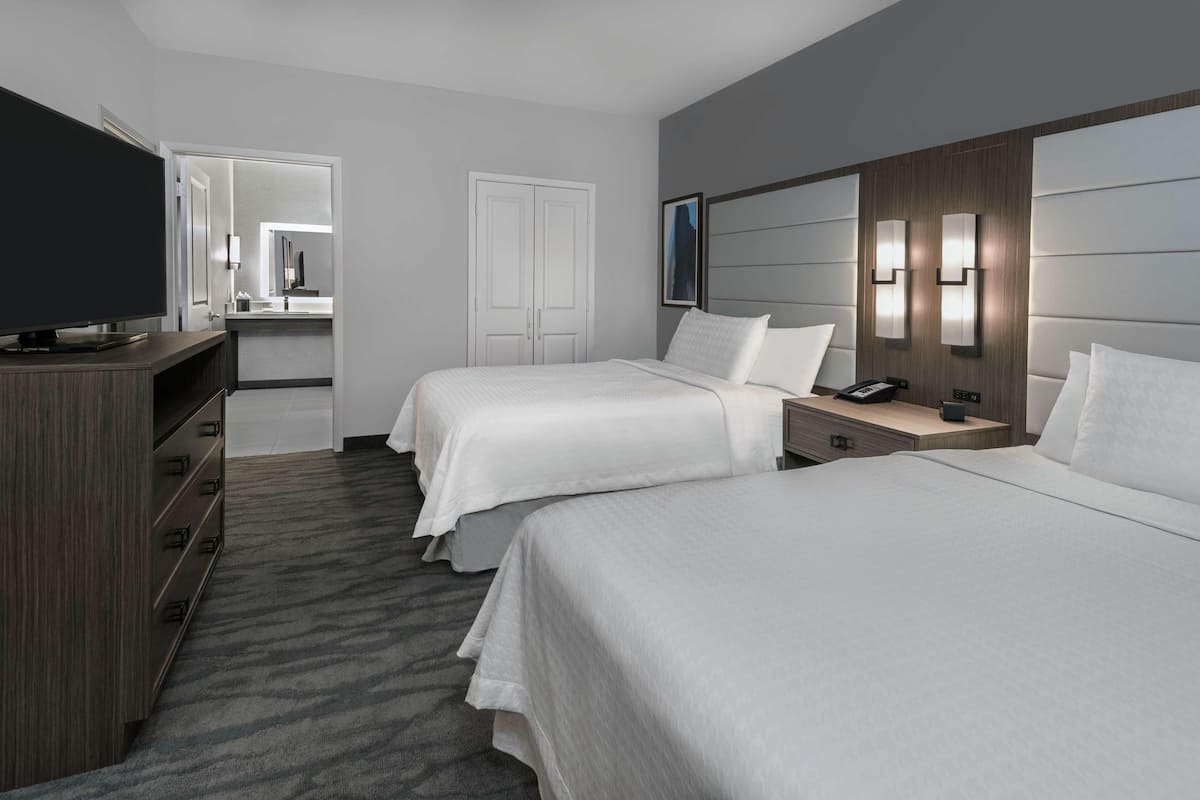 A hotel room with two beds, a TV, a desk, and a mirror.