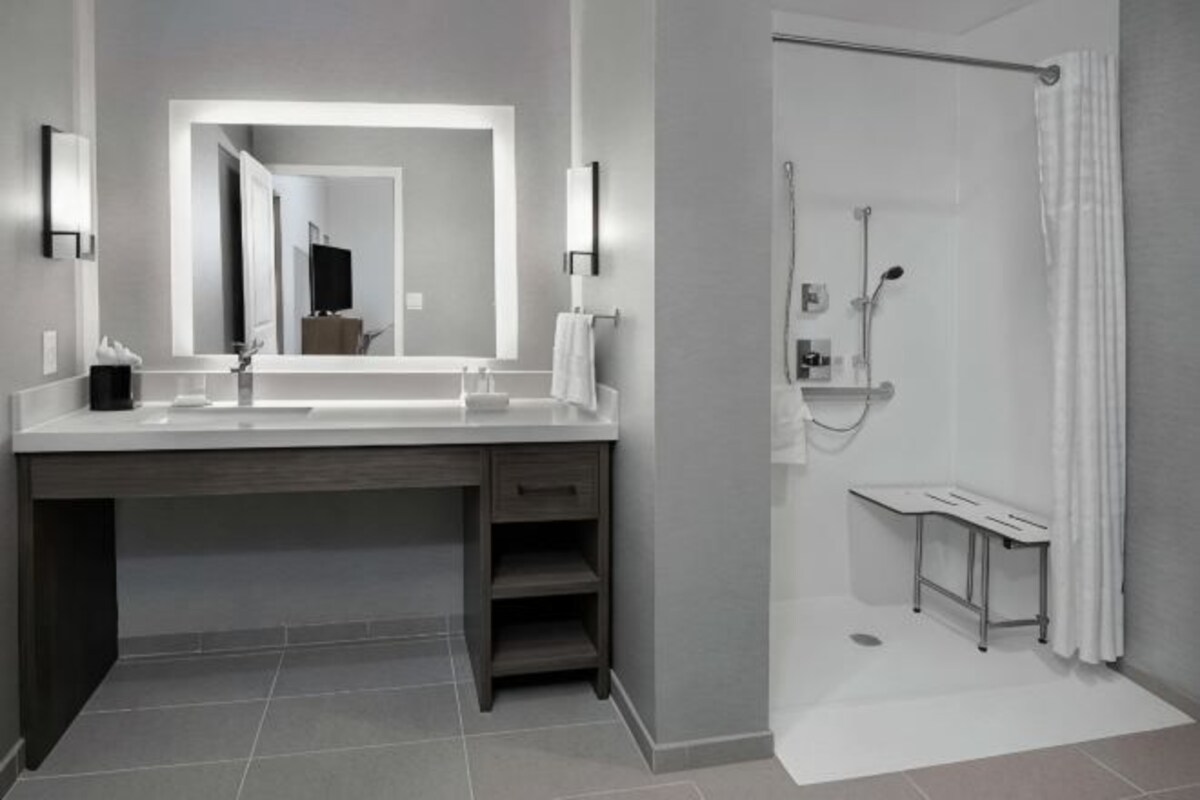 Un baño moderno con un espejo grande, una ducha y un tocador con lavamanos.
