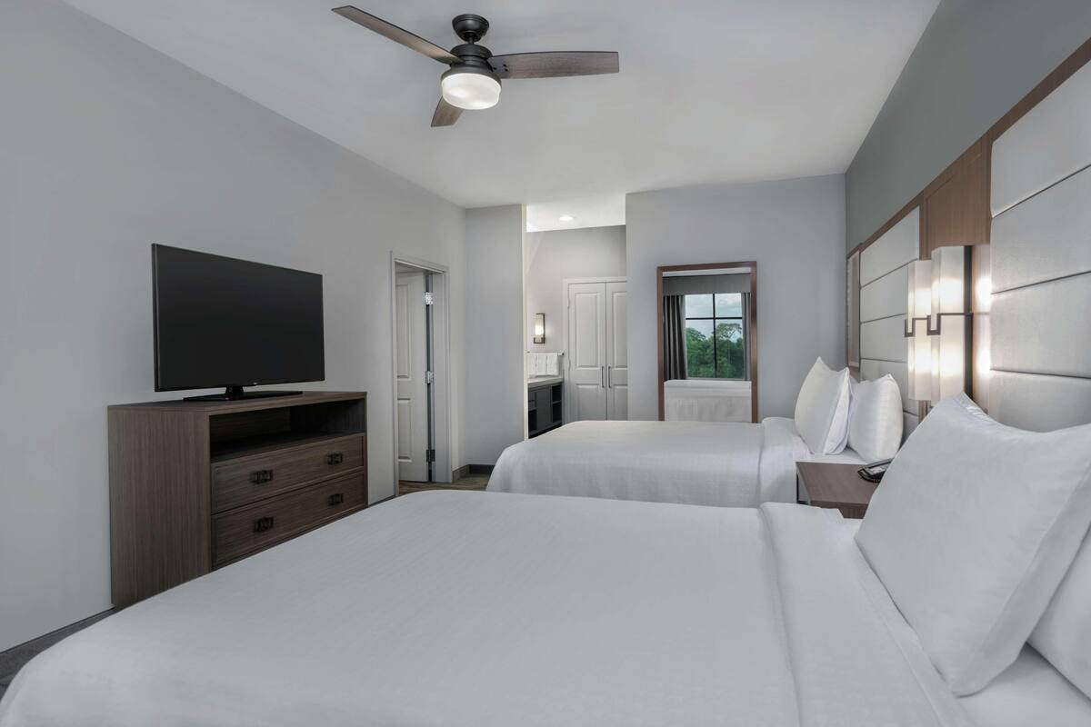 A hotel room with two beds, a TV on a dresser, a ceiling fan, and a window with a view.