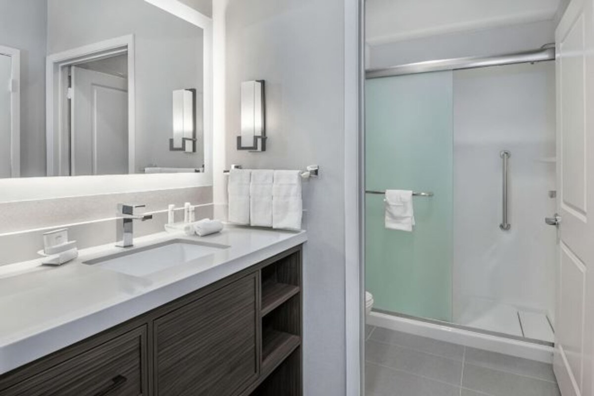 Un baño moderno con un espejo grande, una ducha con puerta de vidrio y un tocador con lavamanos y toallero.