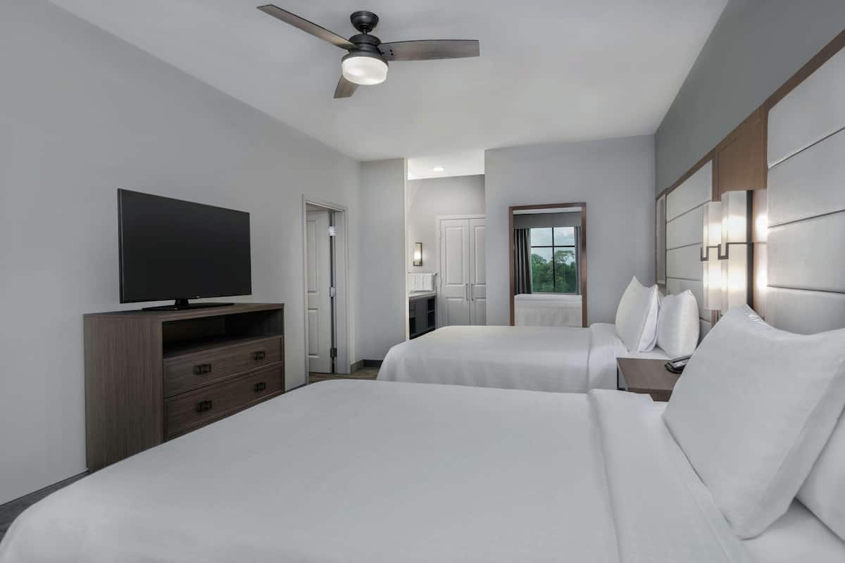 A hotel room with two beds, a TV on a dresser, a ceiling fan, and a window with a view.