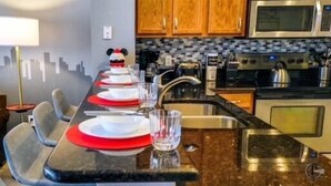 Zona pranzo con un tavolo lungo apparecchiato per quattro persone, un murale con una veduta cittadina e una cucina con elettrodomestici moderni.