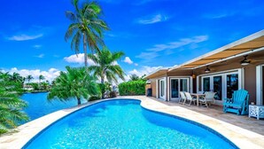A swimming pool with a clear blue water, surrounded by palm trees and a covered patio area with outdoor furniture. - EXQUISITE HEATED POOL+WATERFRONT! 1 MILE TO BEACH! (Pompano Beach)