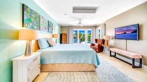 A spacious bedroom with a large bed, a TV, a bench, and artwork on the walls. - EXQUISITE HEATED POOL+WATERFRONT! 1 MILE TO BEACH! (Pompano Beach)