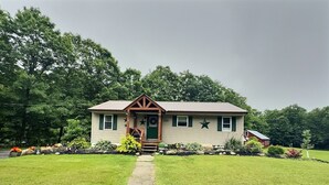 A two-story house with a front porch, a small garden, and a pathway leading to the entrance. - The Perfect Private Escape (Lorraine)