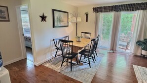 A dining area with a wooden table and chairs, a rug, and a window with curtains. - The Perfect Private Escape (Lorraine)