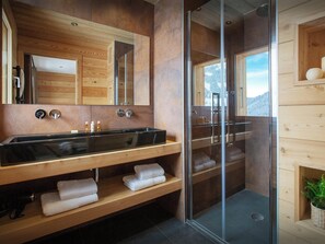A modern bathroom with a wooden vanity, a large mirror, a glass shower enclosure, and a view of the outdoors.