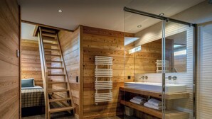 Een moderne badkamer met houten lambrisering, een douchecabine van glas en een vaste ladder naar een slaapkamer op een entresol.
