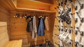 Een houten interieur met een kledingrek, een schoenenrek en een ski-rek aan de muur.