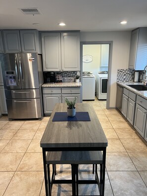A modern kitchen with grey cabinets, stainless steel appliances, and a central island with a potted plant.
