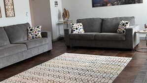 A living room with two grey sofas, a patterned rug, a ceiling fan, and a wall-mounted painting of a canyon. - Close to Sedona, Cottonwood, Wineries & Jerome (Cottonwood)