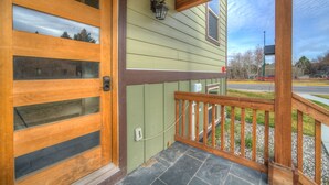 A wooden front door with glass panels, a green exterior wall, and a stone-paved porch with a wooden railing. - Lovely 3 bedroom Apartment in Bozeman! Unit #C  (Bozeman)