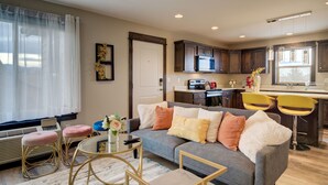 A modern living room with a grey sofa, a coffee table, and a TV. There is a kitchen area with a microwave and a sink. - Lovely 3 bedroom Apartment in Bozeman! Unit #C  (Bozeman)