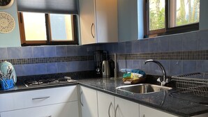 A modern kitchen with white cabinets, a black countertop, a stainless steel sink, and a window with a view of greenery. - Blue Villa Aruba (Oranjestad)