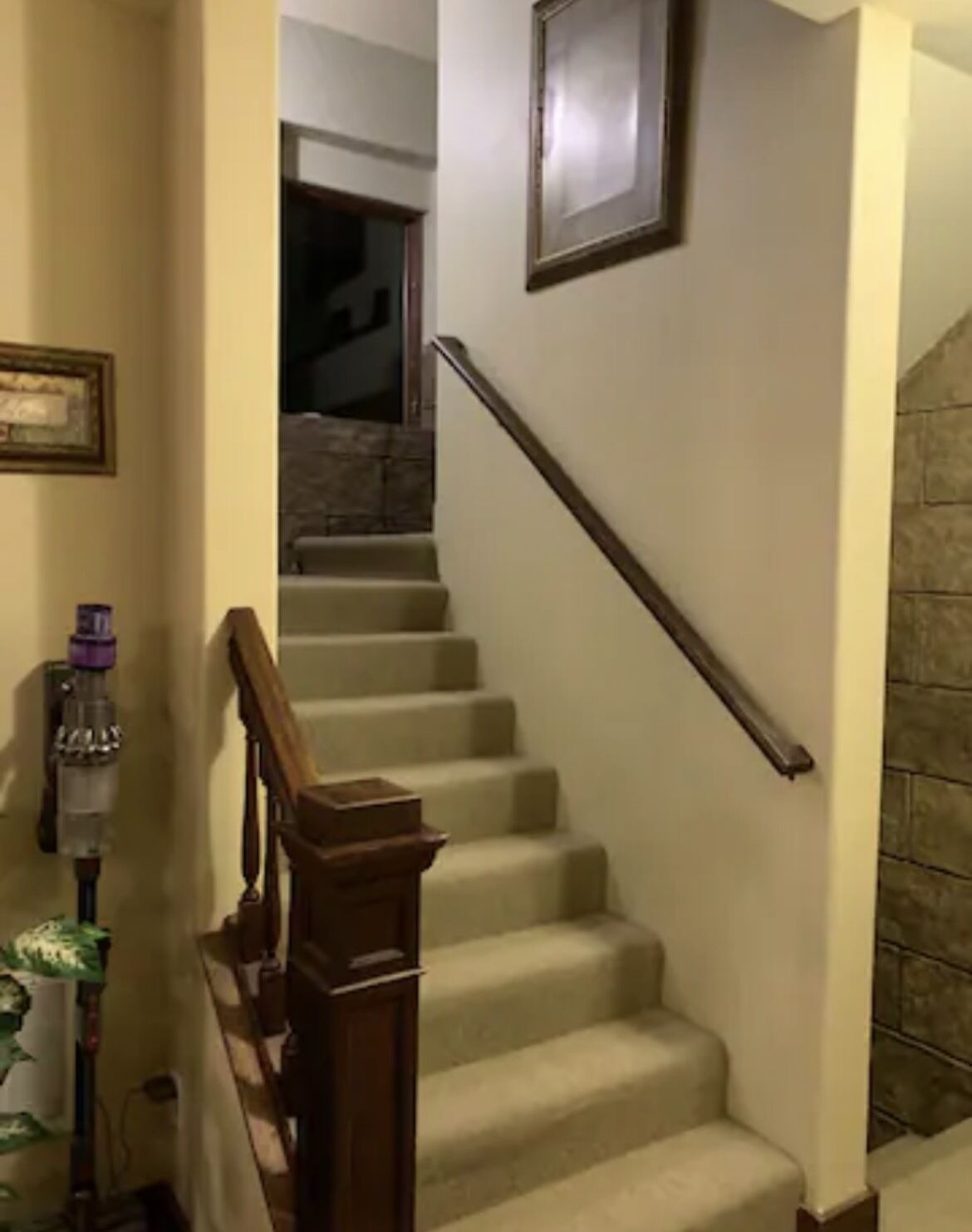 Eine Treppe mit hölzernem Geländer und beige gefliesten Stufen, die zu einer Zwischenebene führen.