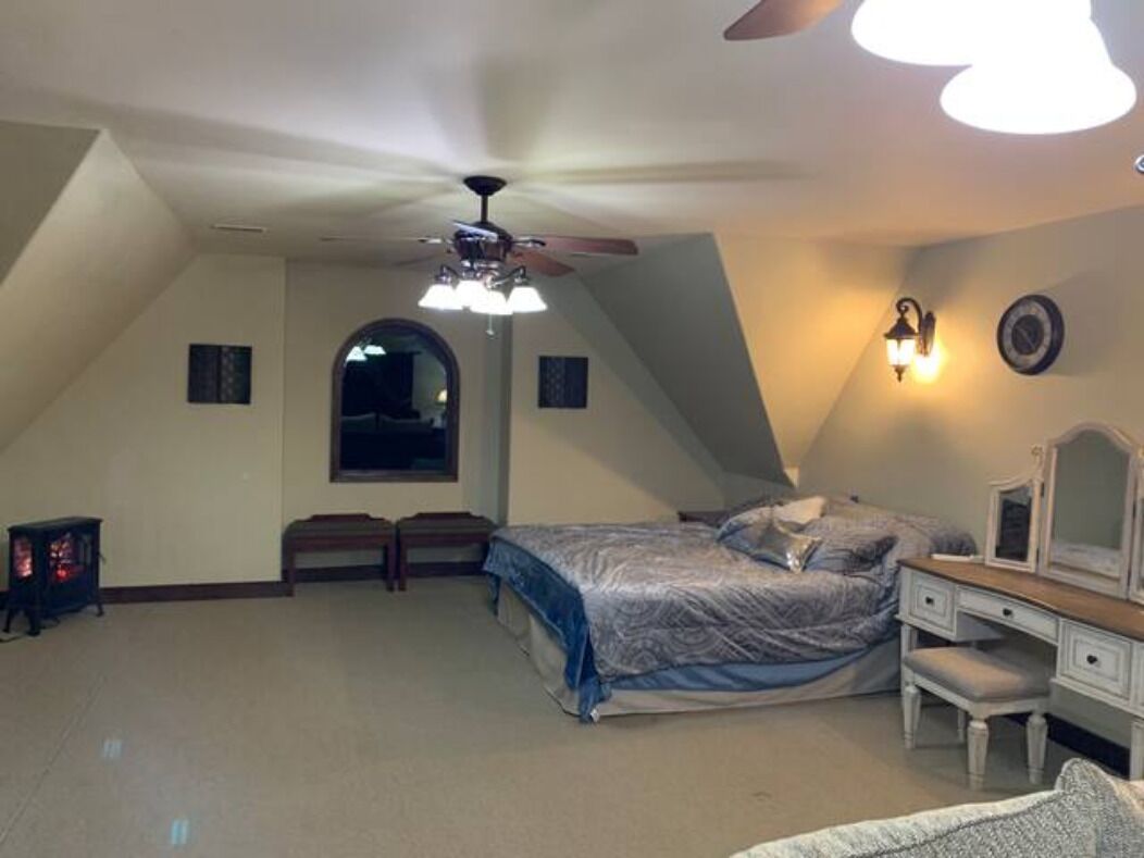 A bedroom with a sloped ceiling, a bed, a dresser, a vanity, and a ceiling fan.
