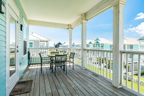 Un porche cubierto con mesa y sillas, terraza de madera y vistas a casas vecinas.