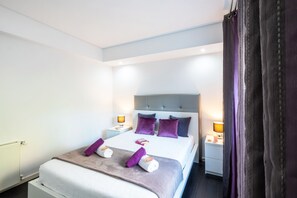 A neatly made bed with a headboard, two bedside tables with lamps, and a window with curtains.