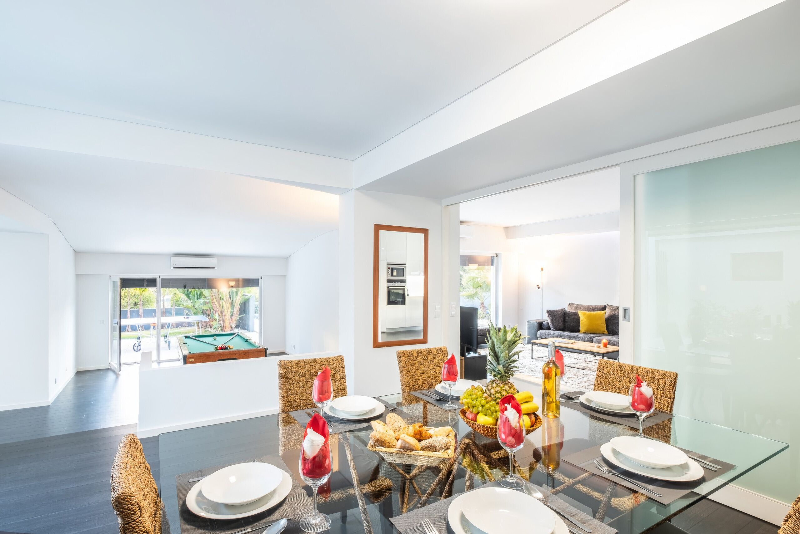 Un espace repas moderne avec une table en verre, des chaises en osier et une vue sur une piscine et un espace extérieur.