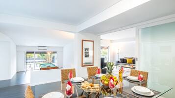Un espace repas moderne avec une table en verre, des chaises en osier et une vue sur une piscine et un espace extérieur.