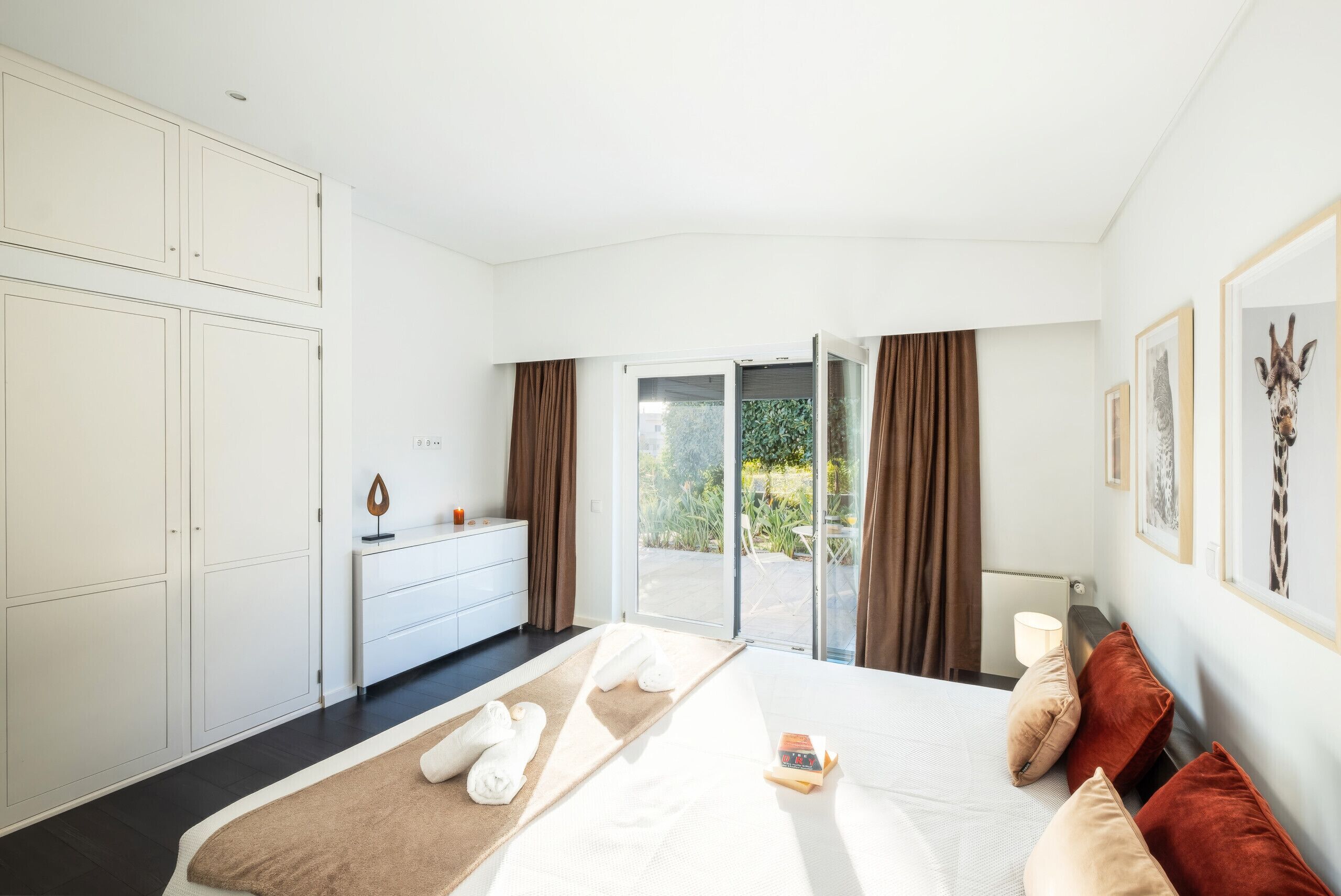 A modern bedroom with a large bed, a dresser, and a sliding glass door leading to a balcony.