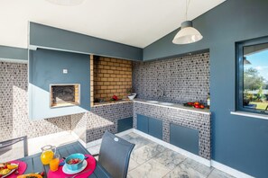 A modern kitchen with a built-in grill, a dining area with a table set for breakfast, and a view through a window.