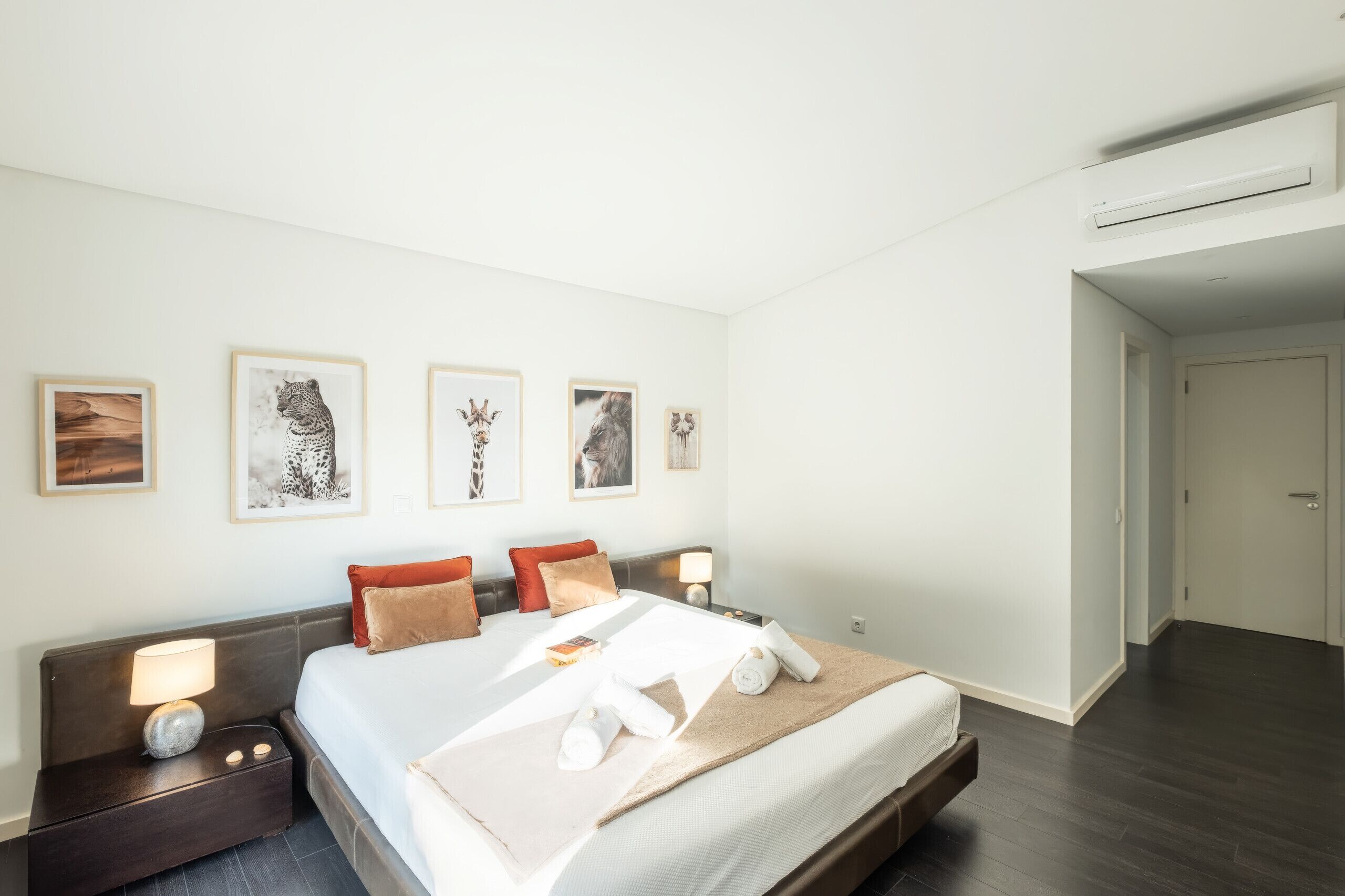 A hotel room with a bed, bedside tables, a nightstand, and wall-mounted artwork.