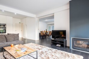 Un soggiorno moderno con una televisione a schermo piatto, un camino, un'area pranzo e una cucina con elettrodomestici integrati.