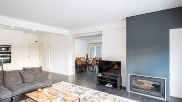 A modern living room with a sofa, coffee table, fireplace, and a dining area in the background.