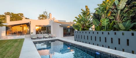A modern house with a swimming pool, outdoor seating, and lush greenery.