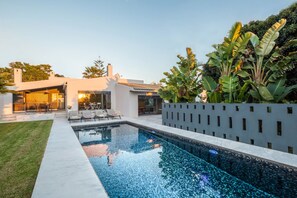 Ein modernes Haus mit Swimmingpool, Sitzgelegenheit im Freien und üppigem Grün.