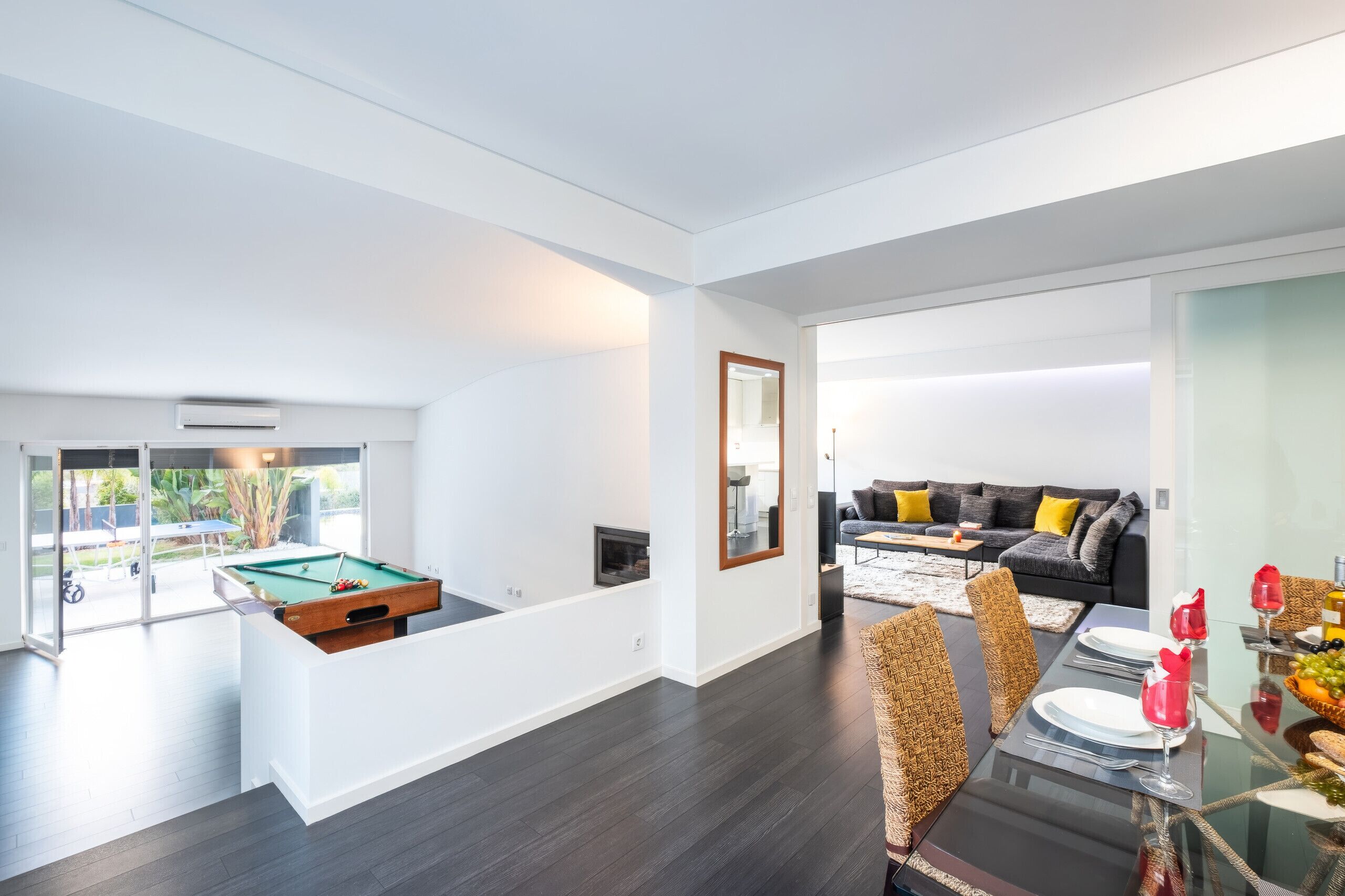 A modern living space with a pool table, a sofa, and a dining area with a glass table.