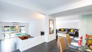 A modern living space with a pool table, a sofa, and a dining area with a glass table.