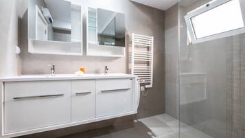 A modern bathroom with a white vanity, a glass shower enclosure, and a built-in towel rack.