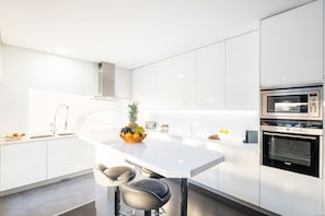Een moderne keuken met witte kasten, een centraal eiland met zitplaatsen en inbouwapparatuur, waaronder een magnetron en oven.
