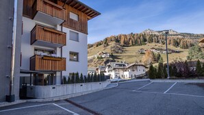 Ein modernes Gebäude mit hölzernen Balkonen, einem Parkplatz und Blick auf eine hügelige Landschaft mit Häusern.