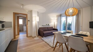 Ein modernes Wohnzimmer mit einer Couch, einem Esstisch und Stühlen. Es gibt eine Küchenzeile mit einer Mikrowelle und einem Kühlschrank.