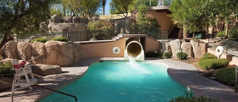 A pool area with a water slide, rock formations, and palm trees.