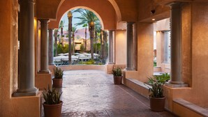 A covered walkway with columns and potted plants, leading to an outdoor area with palm trees and umbrellas. - The Westin Mission Hills Resort Villas, Palm Springs (Rancho Mirage)