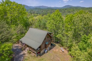 A cabin with a metal roof, surrounded by dense forest and mountains in the background. - Maple Hill Cabin | Pet-Friendly Lake Lure Cabin with Views, Fireplaces & Riverbend Amenities (Lake Lure)