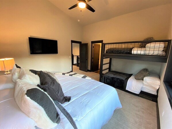Habitación de hotel con una cama grande, una cama nido inferior, un televisor de pantalla plana montado en la pared y un ventilador de techo.