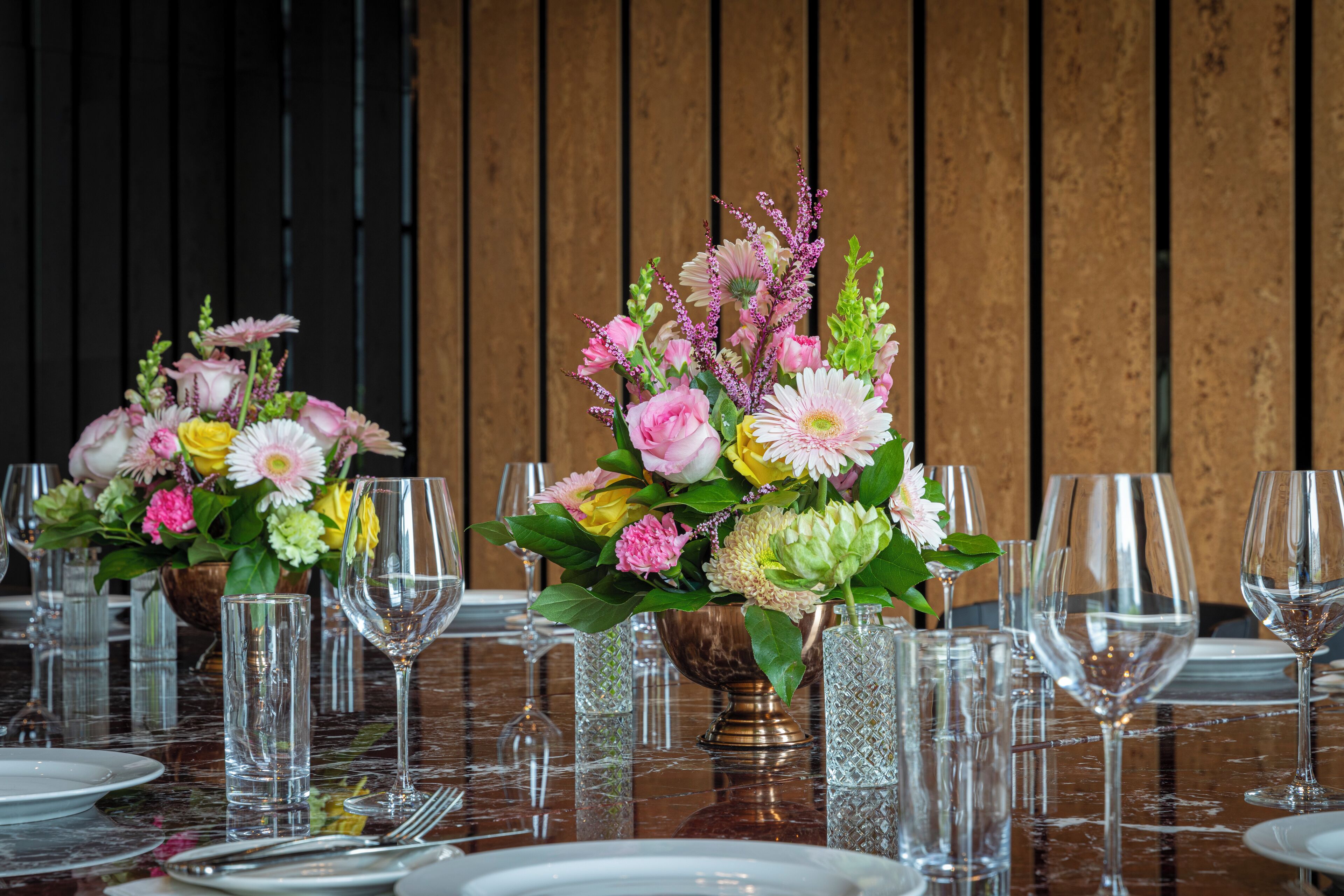 Une table à manger dressée avec de nombreux verres et des centres de table floraux.