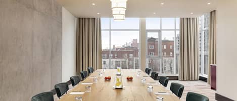 A conference room with a long table, chairs, and a city view through large windows.