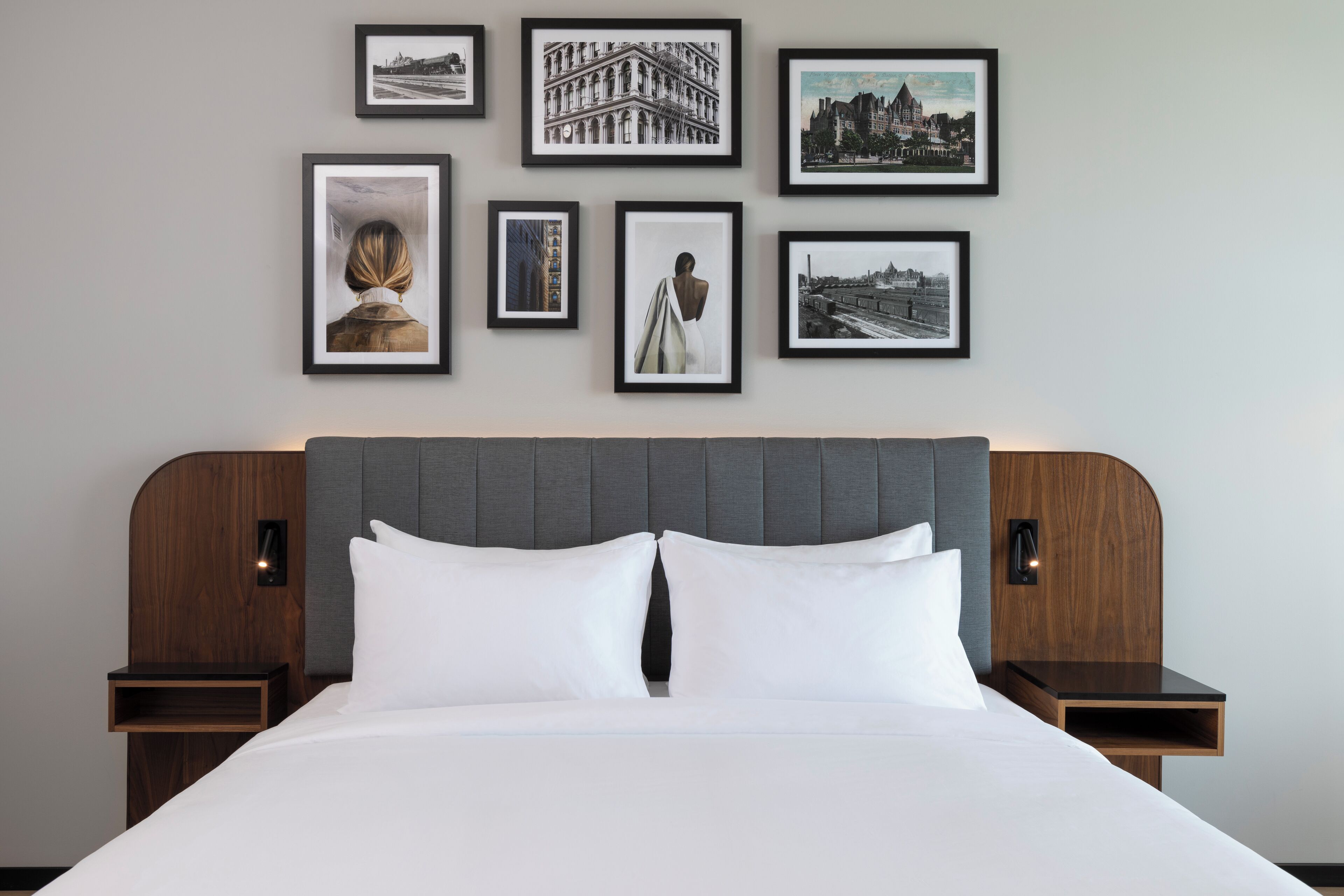 A hotel room with a large bed, two bedside tables, a grey upholstered headboard, and framed pictures on the wall.