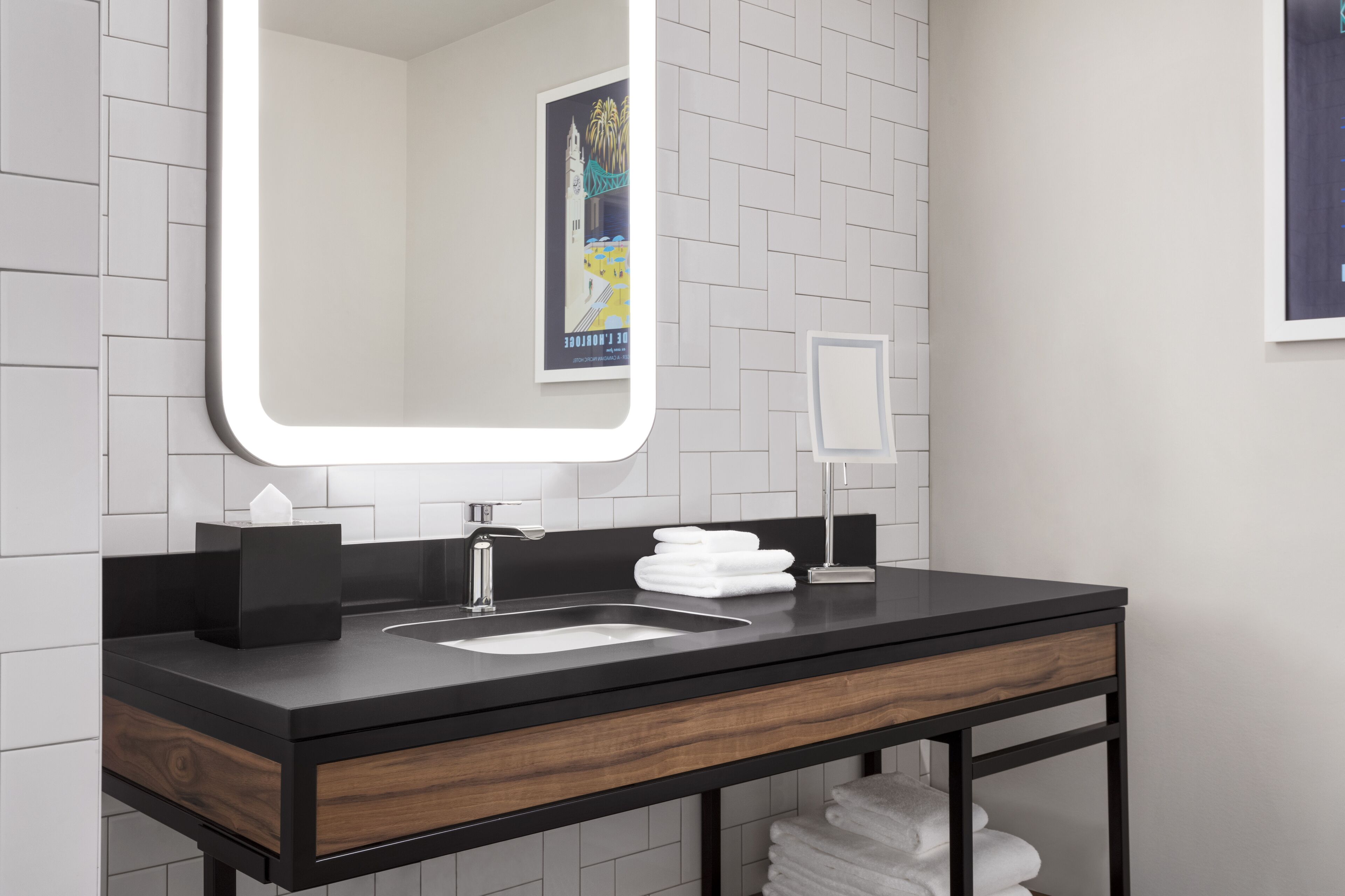 A modern bathroom with a black countertop, a large mirror, a sink, and a wooden drawer.