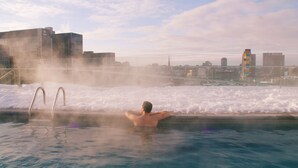 Eine Person in einer Whirlpool-Badewanne, im Hintergrund eine Stadtlandschaft.